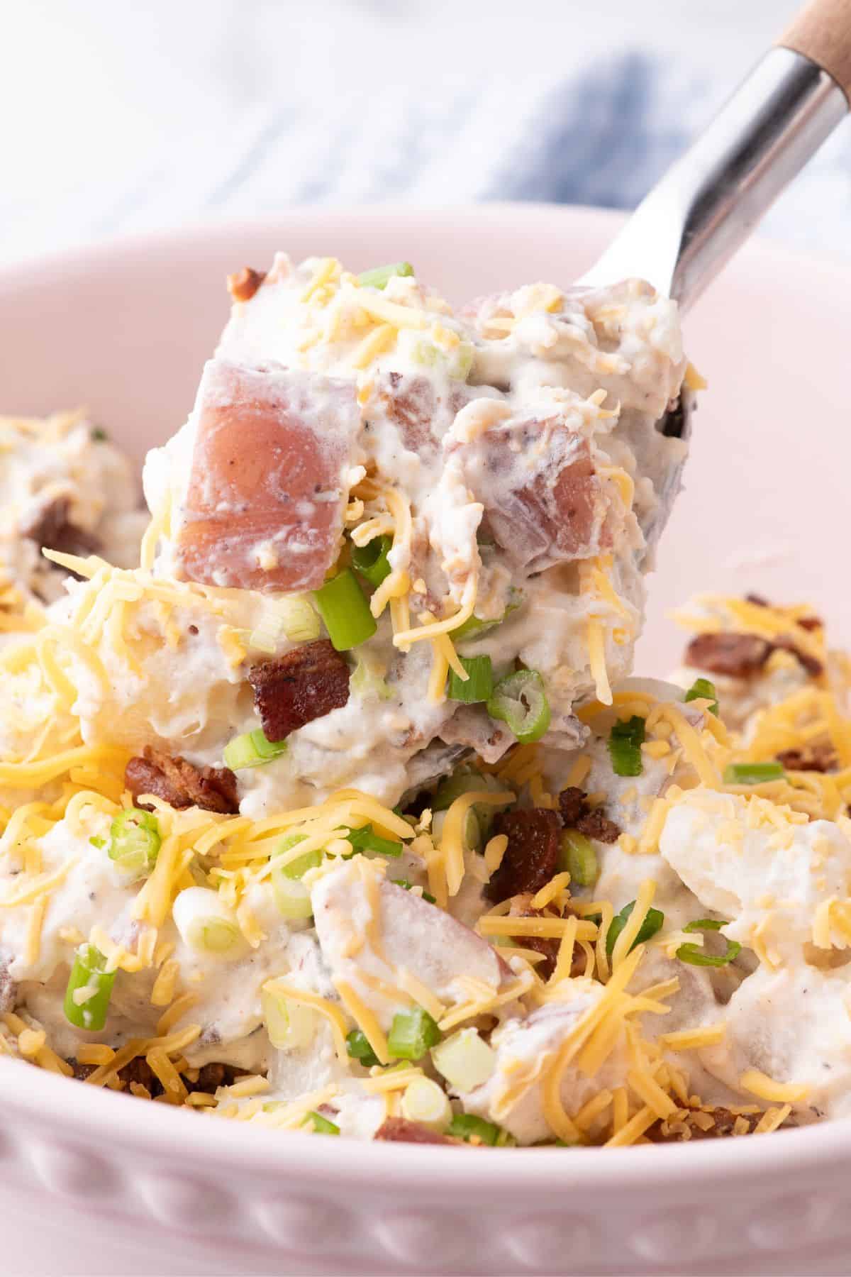 A serving spoon is lifting a serving of loaded potato salad out of the bowl.
