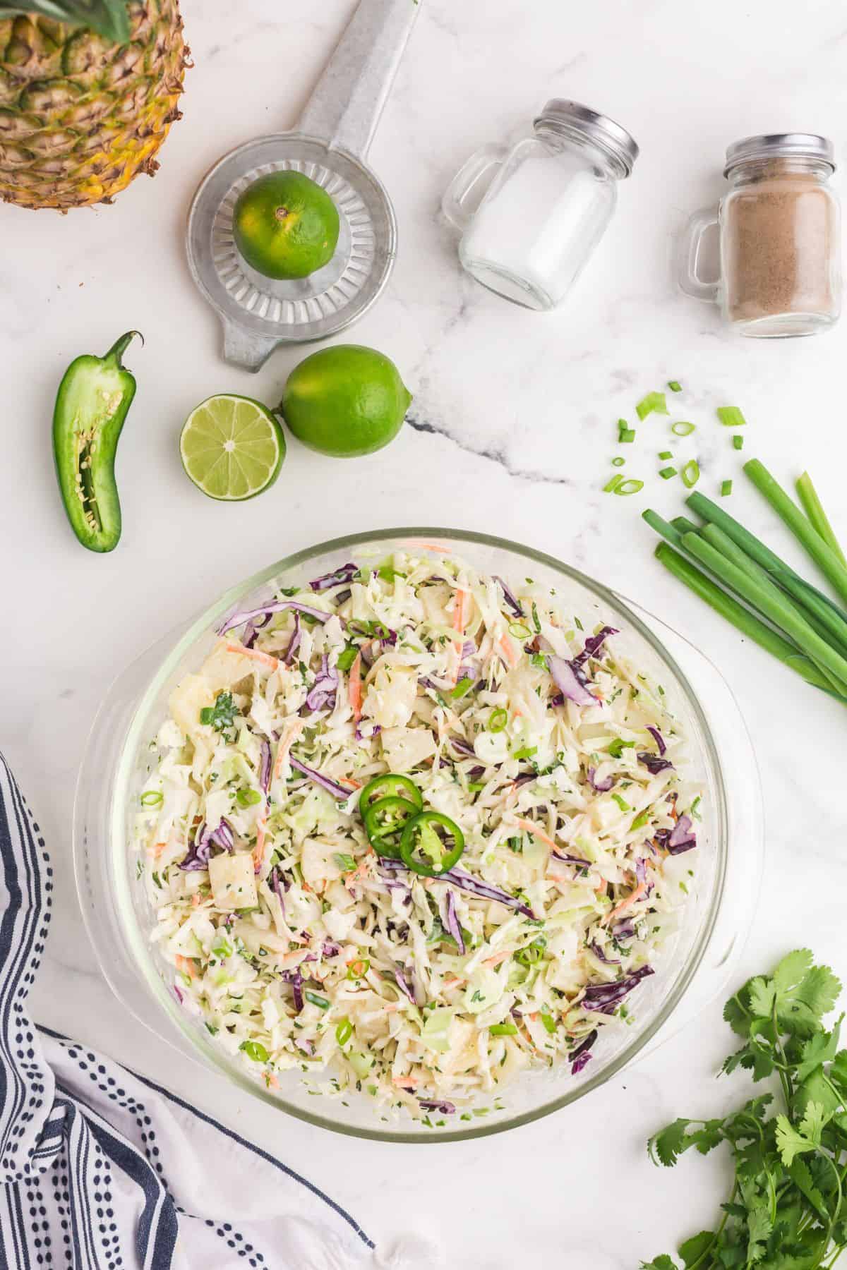 Completed coleslaw in a glass mixing bowl. Salad is garnished with sliced jalapenos.