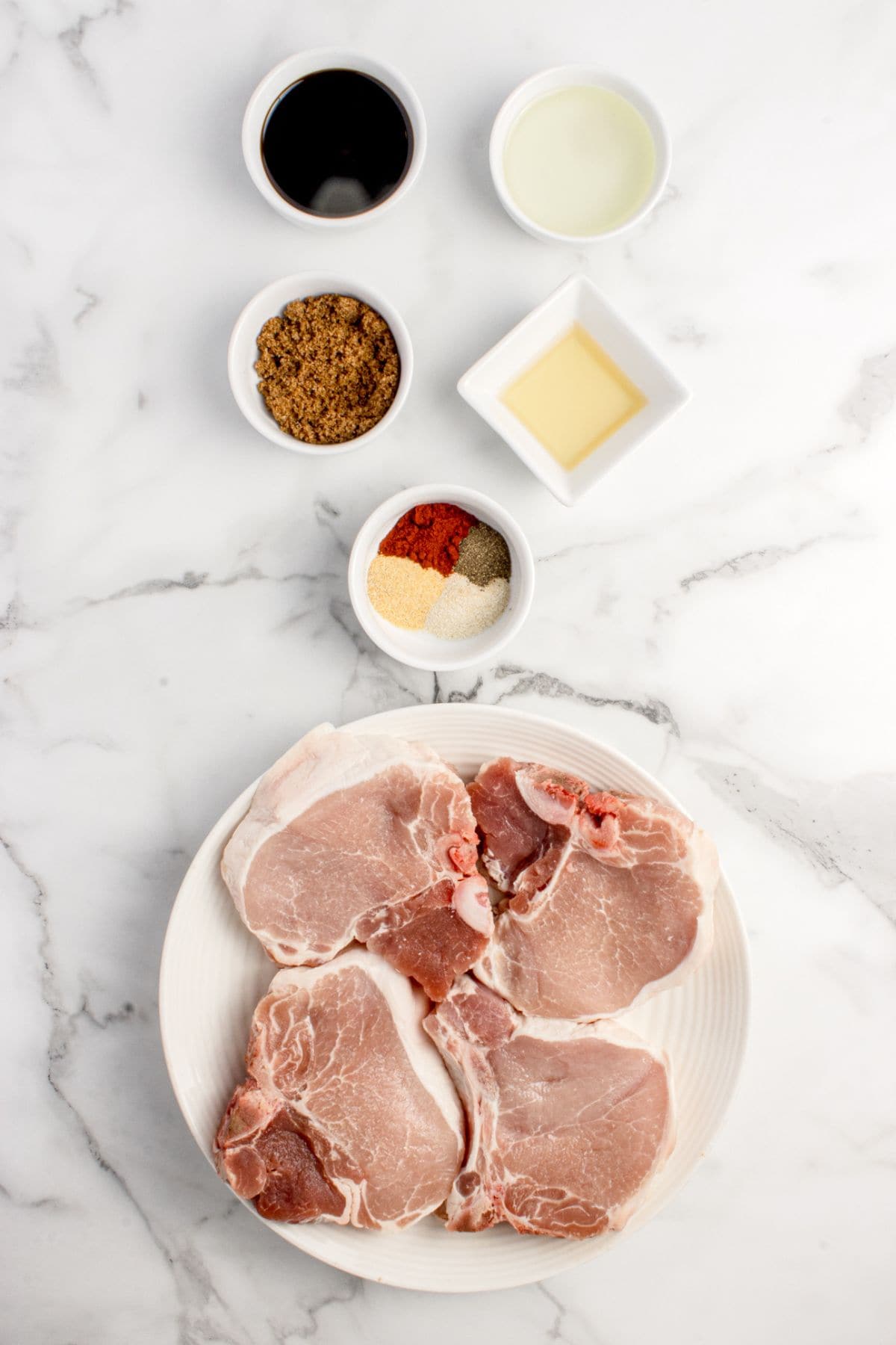 Ingredients for pork chop marinade: neutral oil, brown sugar, apple cider vinegar or lemon juice, soy sauce or tamari, garlic powder, onion powder, black pepper, paprika, and pork chops.