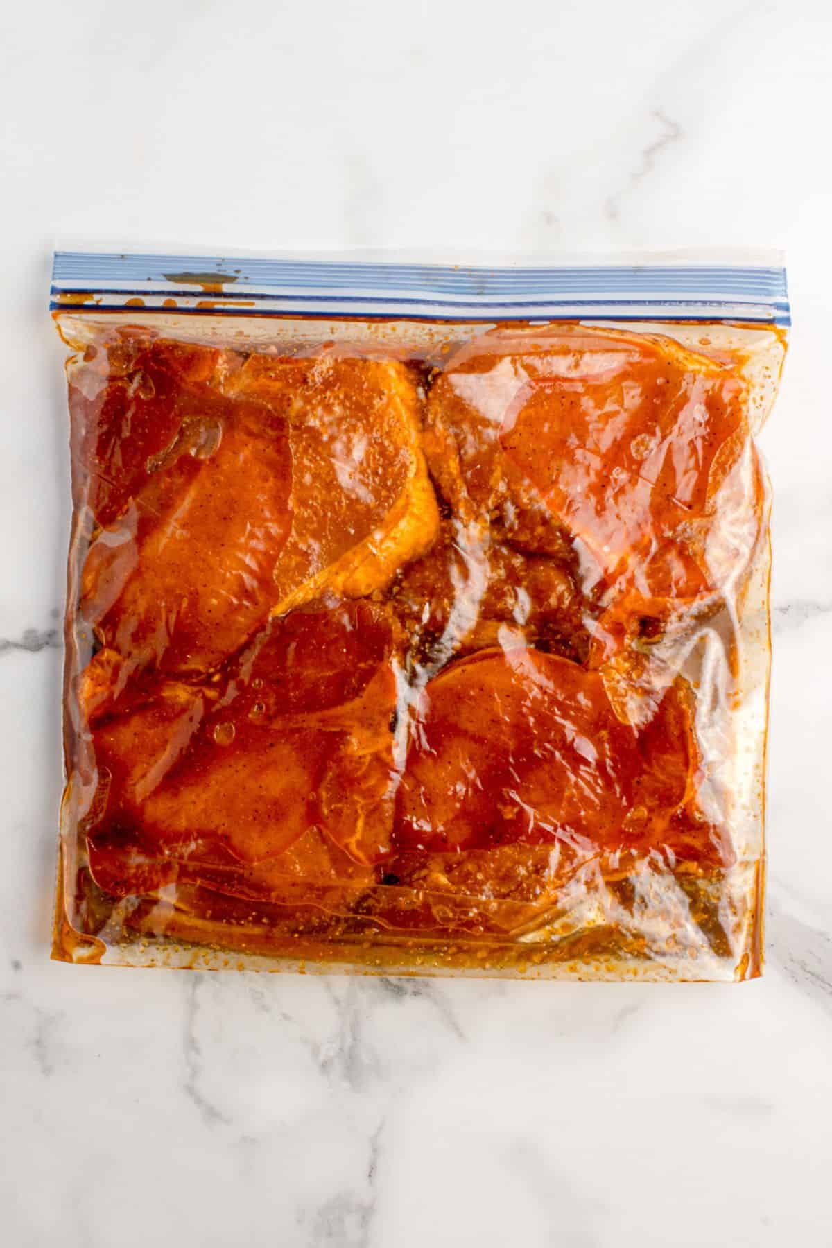 Pork chops marinating in a zip top plastic bag.