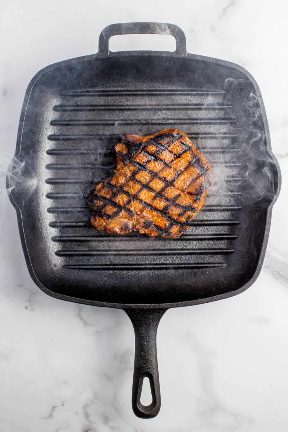 Pork chop searing in a hot grated cast iron pan.