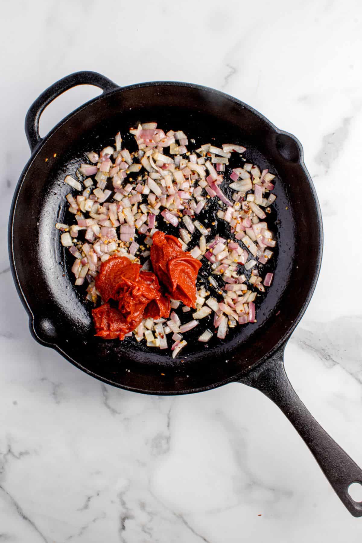 Olive oil, red onion, garlic, red pepper flakes combined with tomato paste in a cast iron pan.