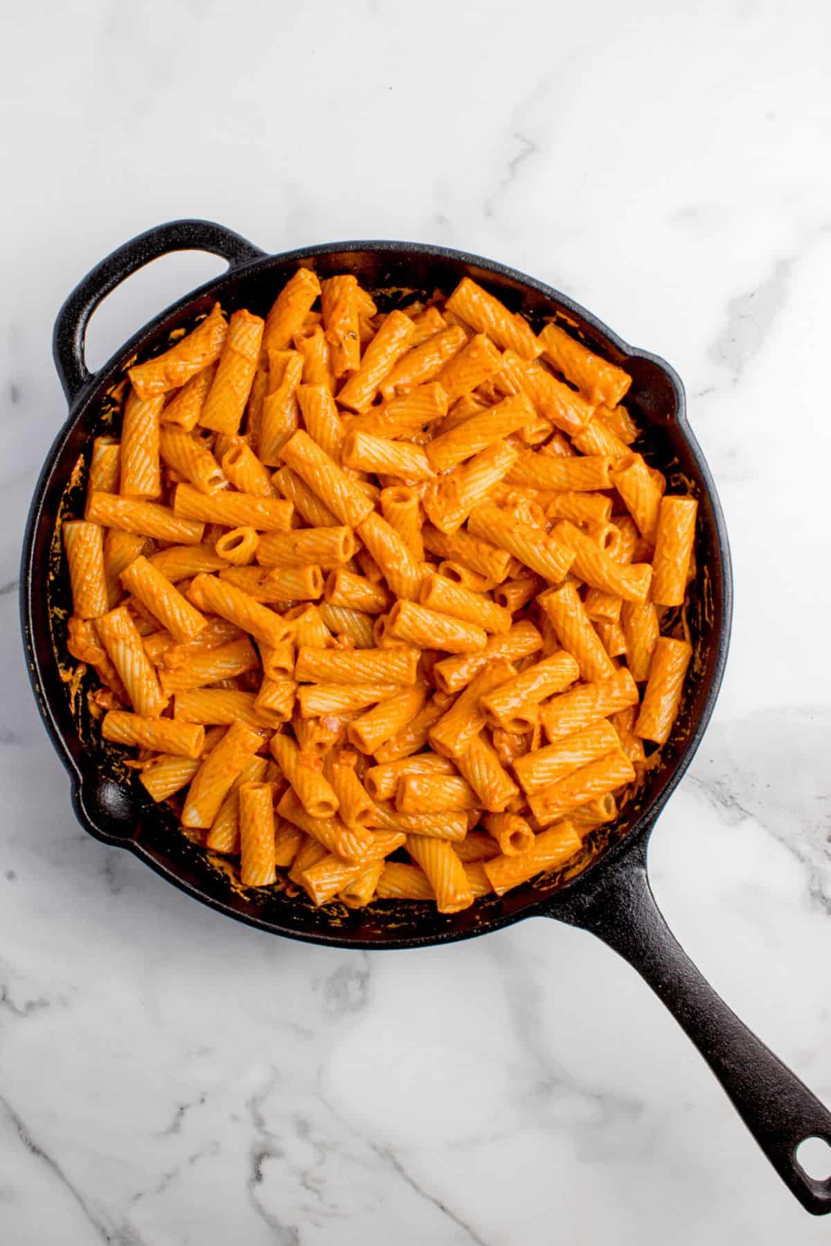 Sauce and pasta are mixed together to complete pasta recipe.