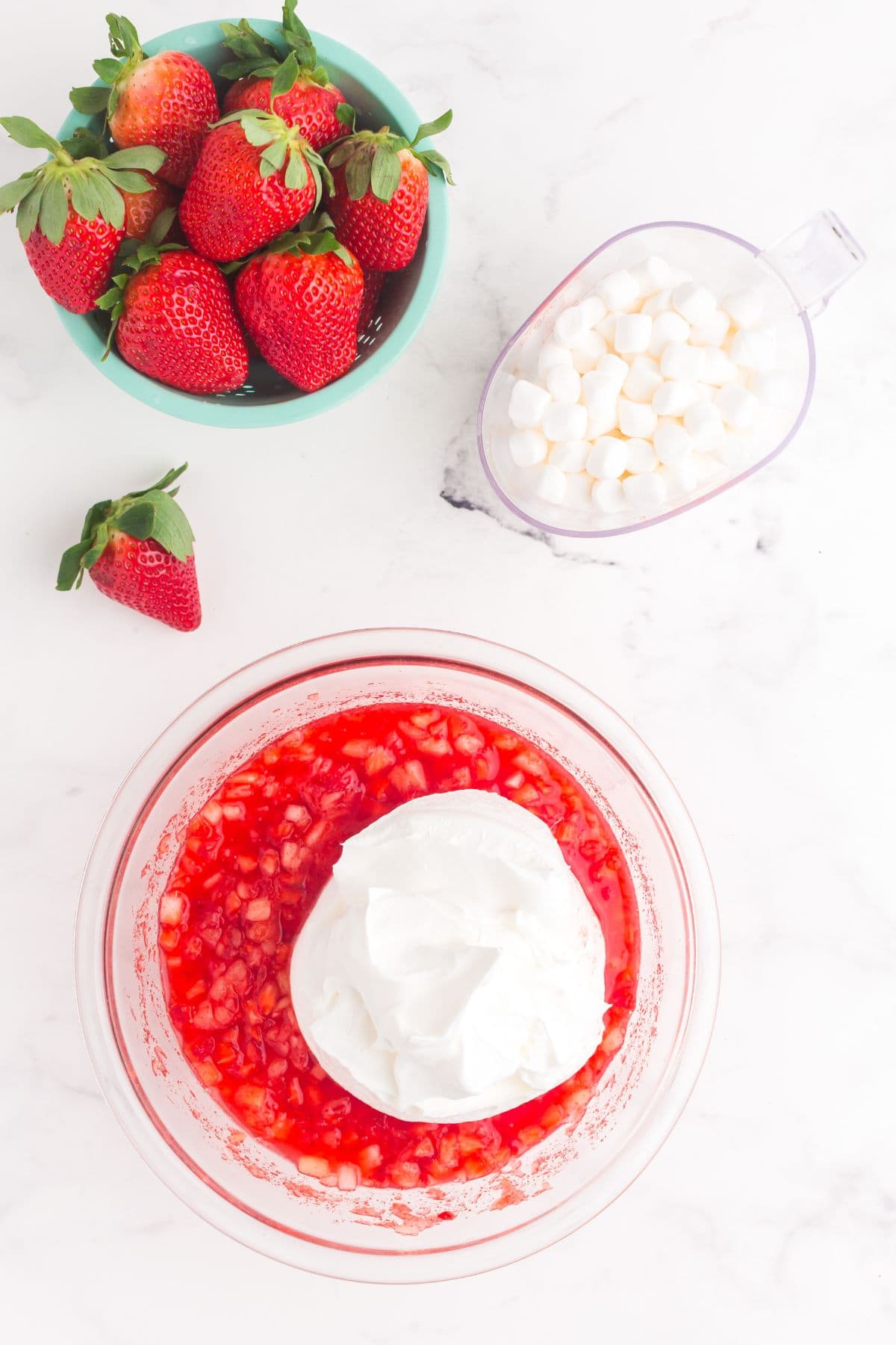 Cool Whip added to the strawberry mixture in a glass mixing bowl.