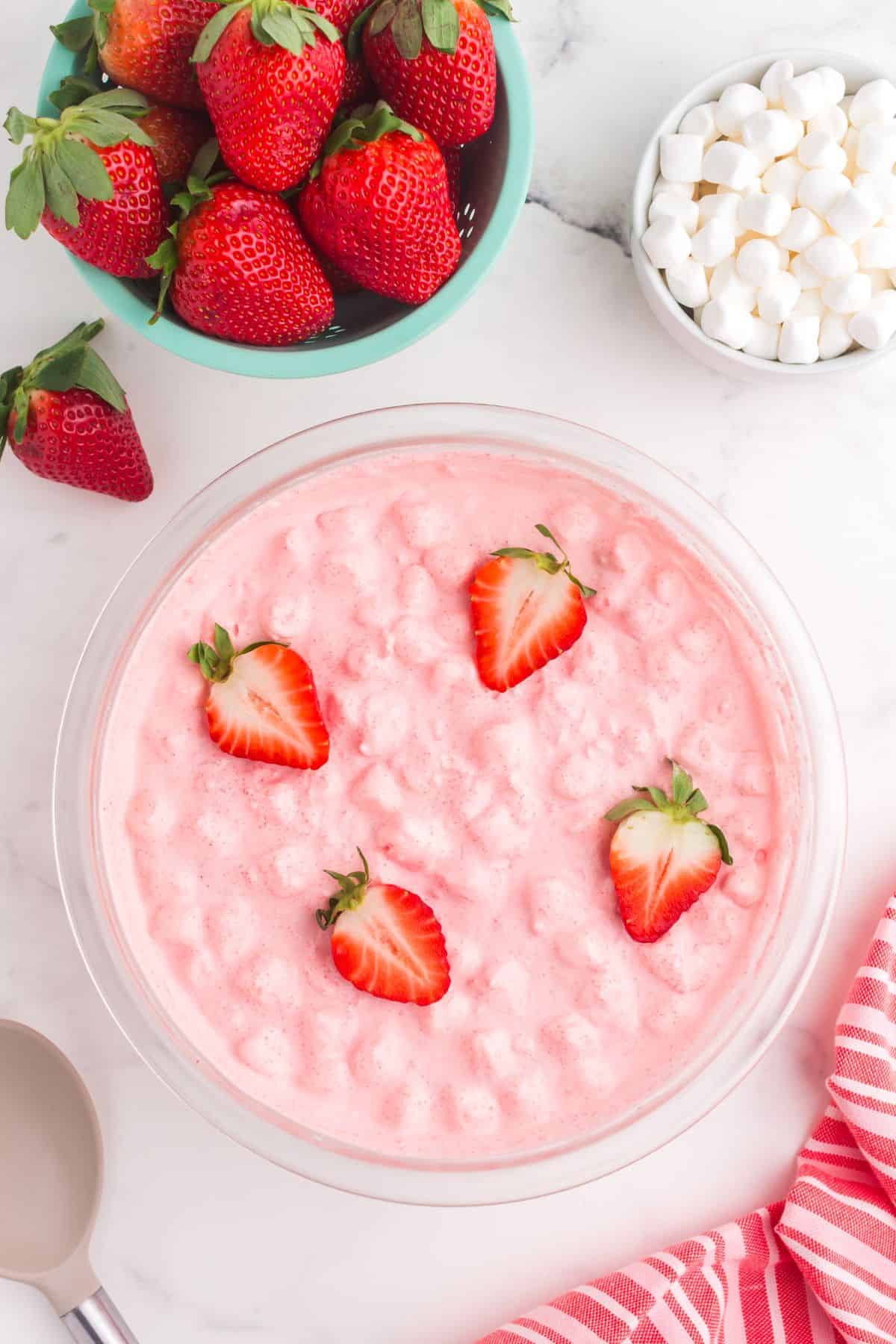 Completed strawberry fluff in a glass bowl. Four strawberry halves are placed on top of the dessert.