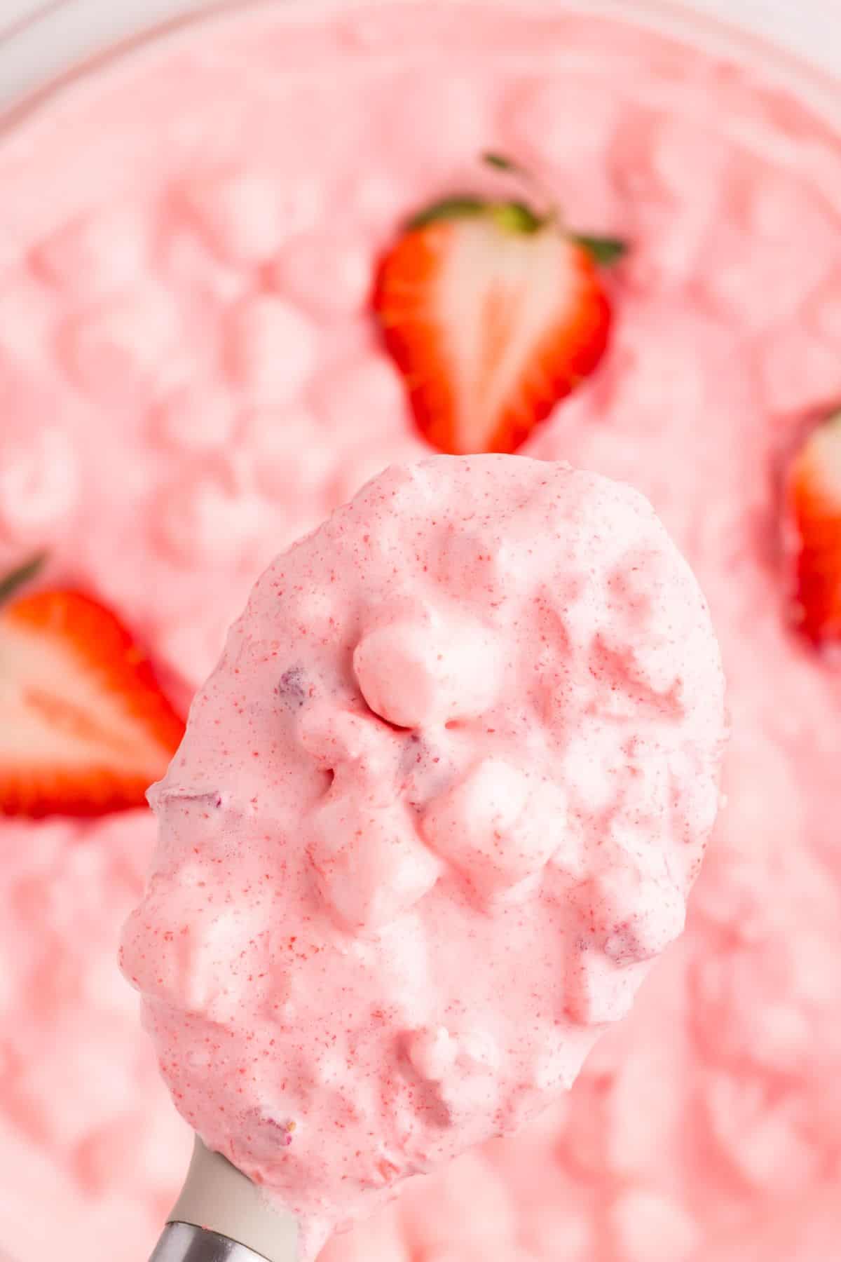 A serving spoon is lifting the strawberry fluff mixture above the bowl.