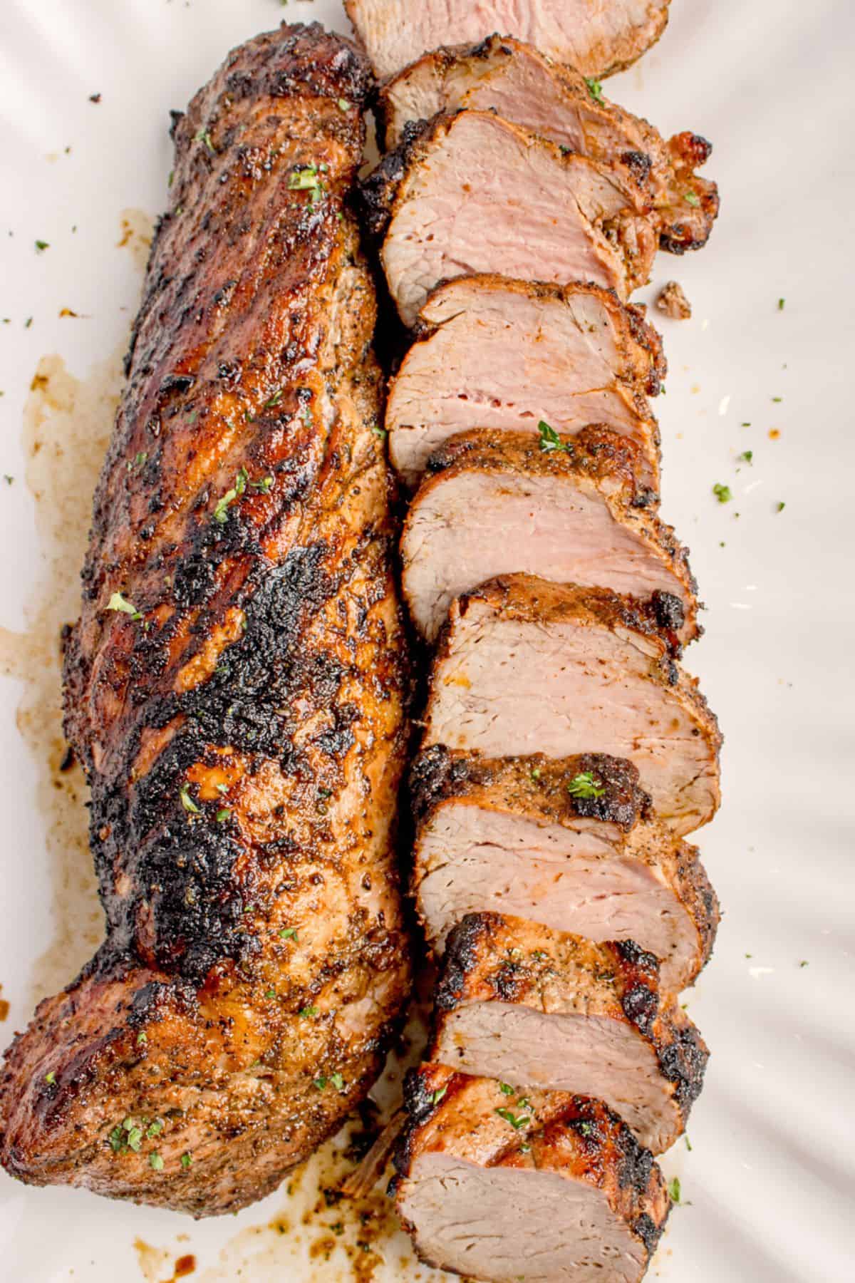 Grilled pork tenderloin with one piece uncut and the other cut into medallions on a white serving platter.