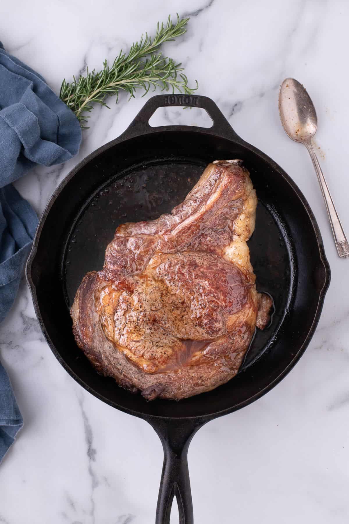Ribeye steak seared on both sides in a cast iron pan.
