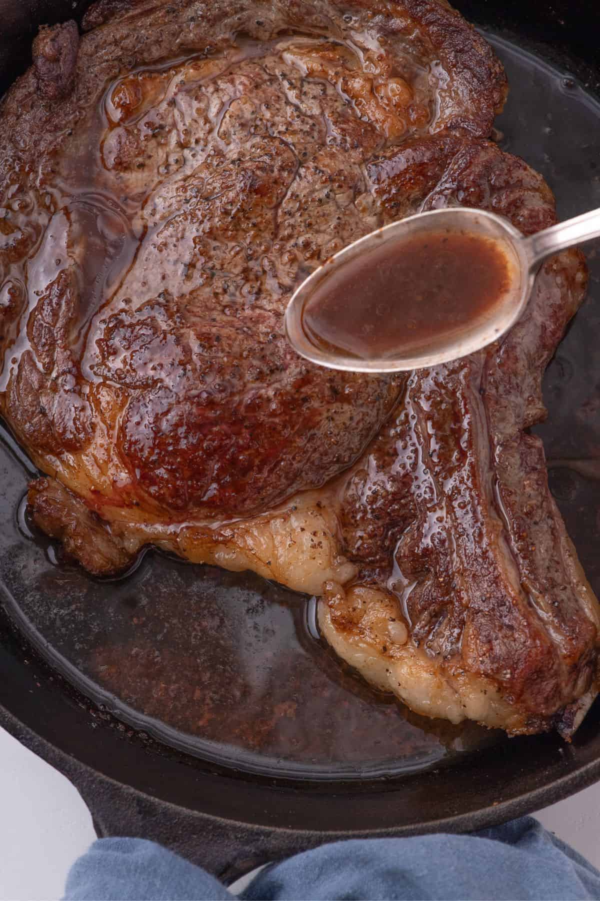 A spoon pouring meat drippings on top of seared steak.