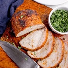Grilled pork loin sliced on a wooden cutting board. Slices are fanned out to show interior texture.