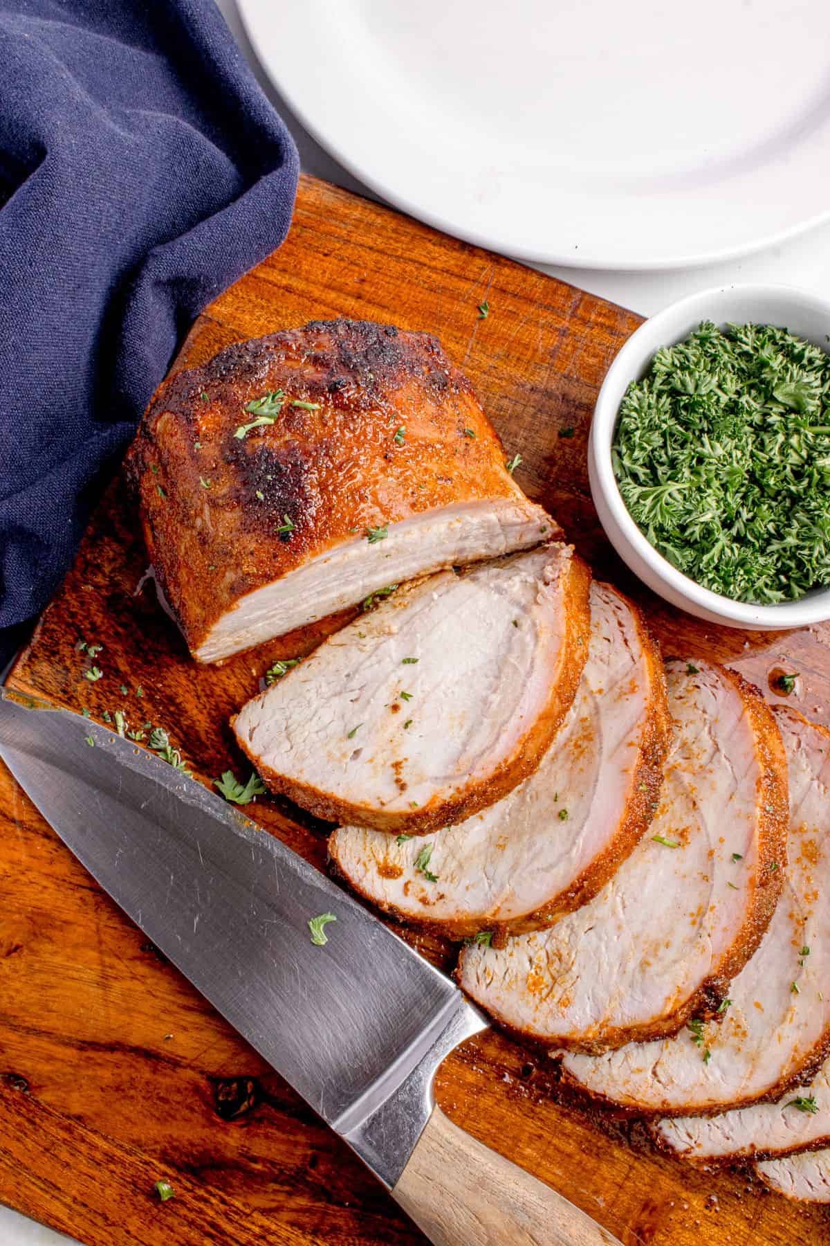 Grilled pork loin sliced on a wooden cutting board. Slices are fanned out to show interior texture.