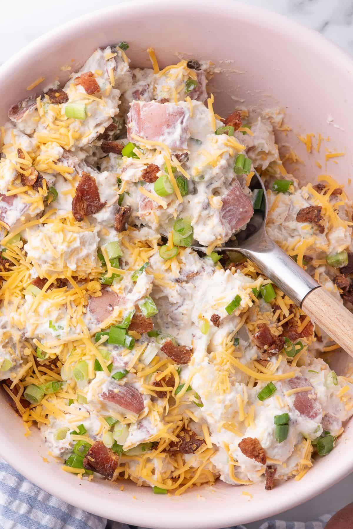Loaded potato salad in a serving bowl with a spoon in it.