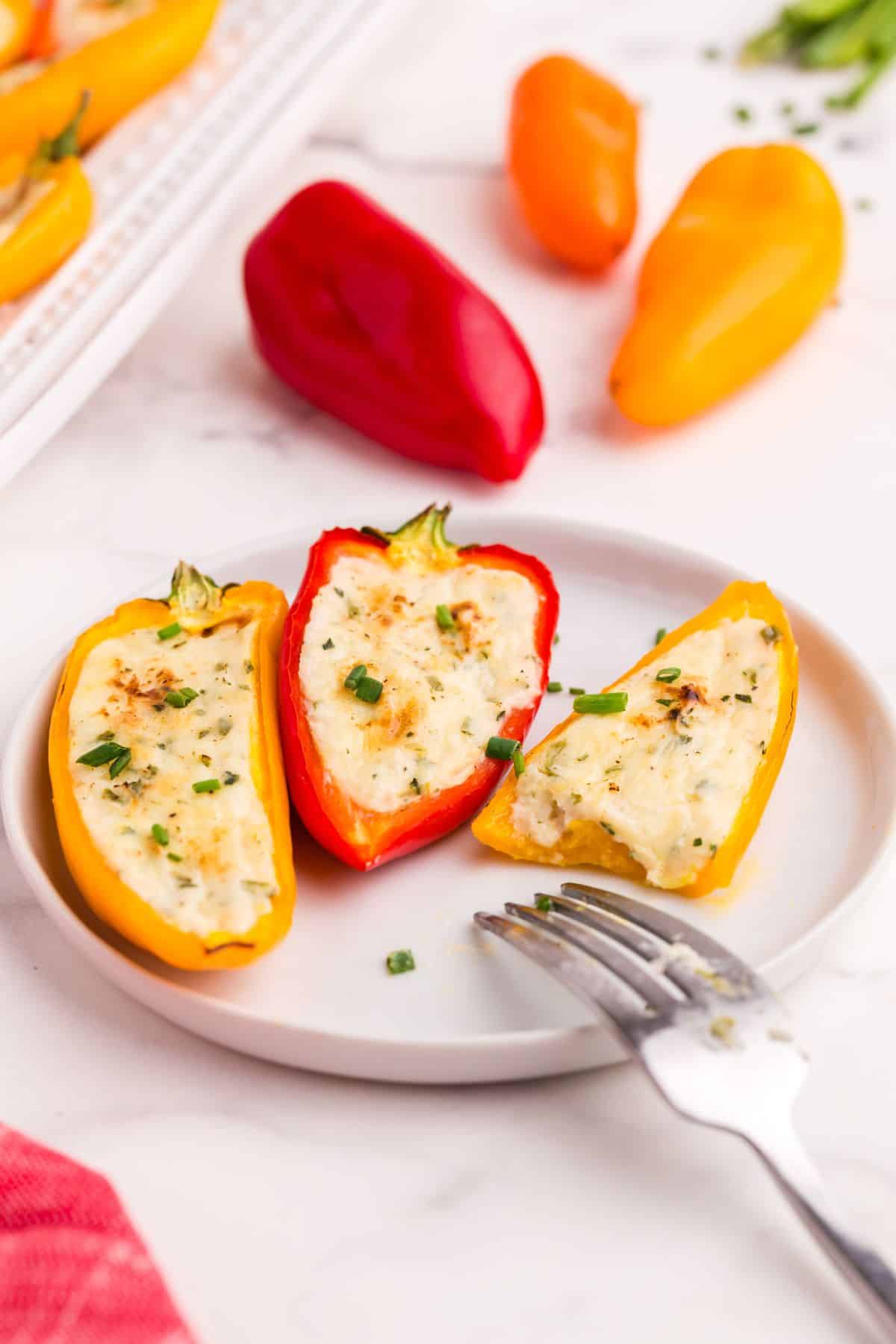 Completed cream cheese stuffed peppers on a white plate with a fork. The yellow pepper on the right has a bite taken out of it.