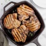 Cast iron pan with cooked and garnished pork chops.