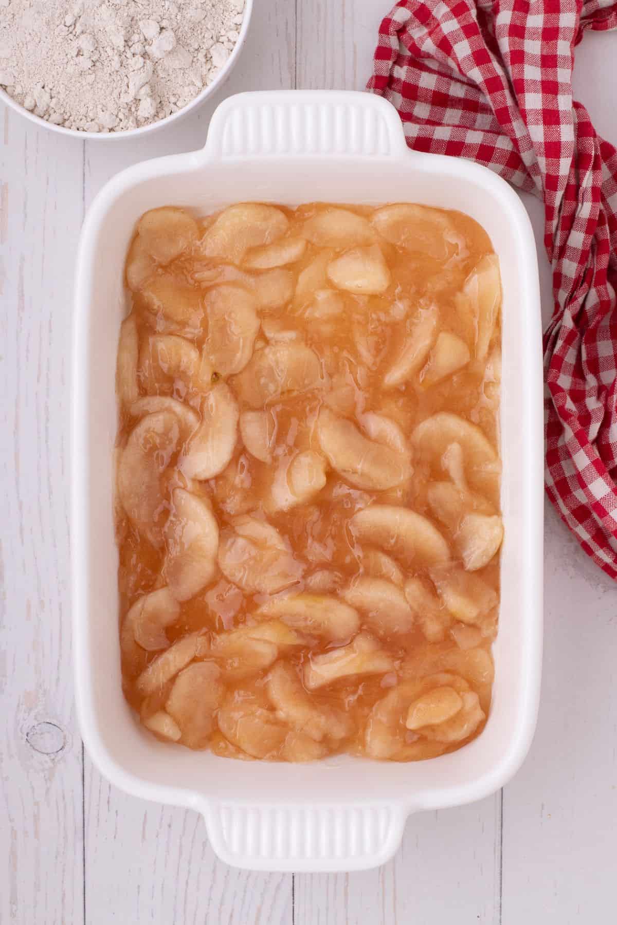 Apple pie filling evenly spread on the bottom of the baking pan.