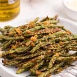 Baked green beans on a serving plate with a large serving fork.