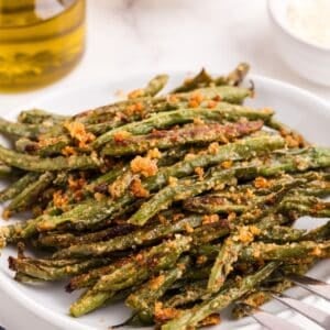 Baked green beans on a serving plate with a large serving fork.