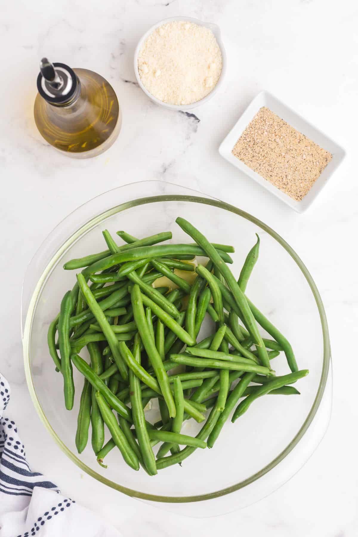 Ingredients for baked green beans: fresh green beans, olive oil, grated parmesan cheese, onion powder, garlic salt, and pepper.