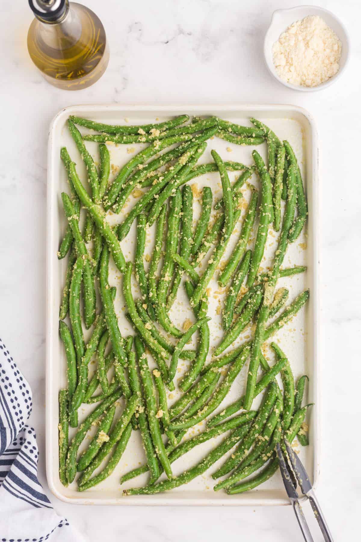 Unbaked, seasoned green beans on a baking sheet.