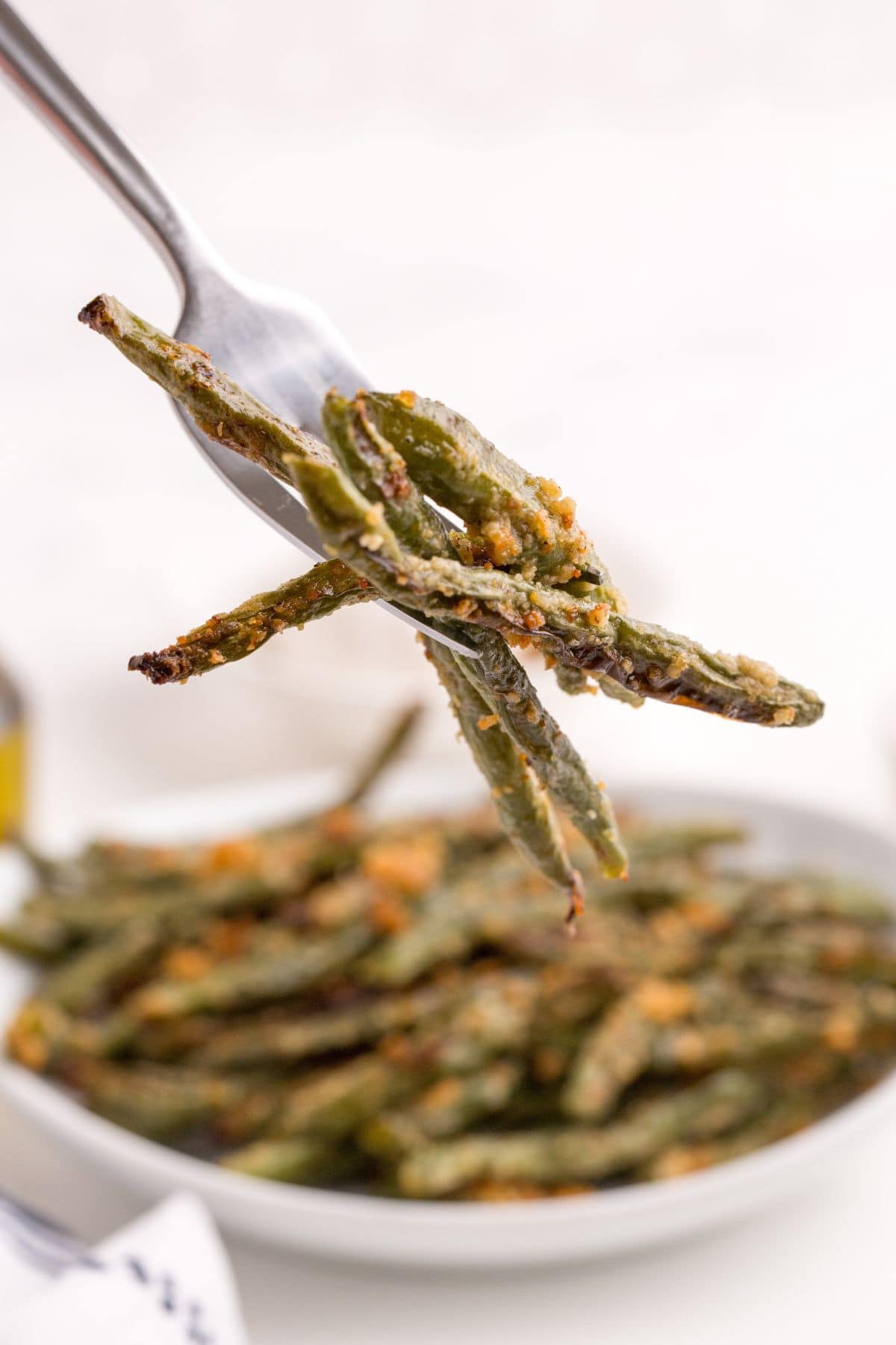 Completed baked green beans on a fork above the plate of green beans.