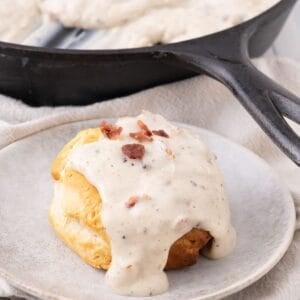 Bacon gravy served over top a biscuit on a taupe stoneware plate.