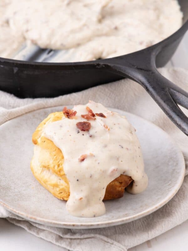 Bacon gravy served over top a biscuit on a taupe stoneware plate.
