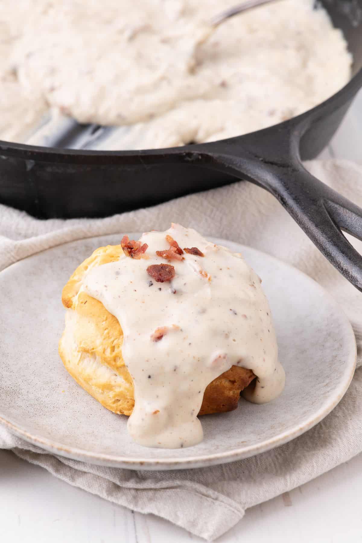 Bacon gravy served over top a biscuit on a taupe stoneware plate.