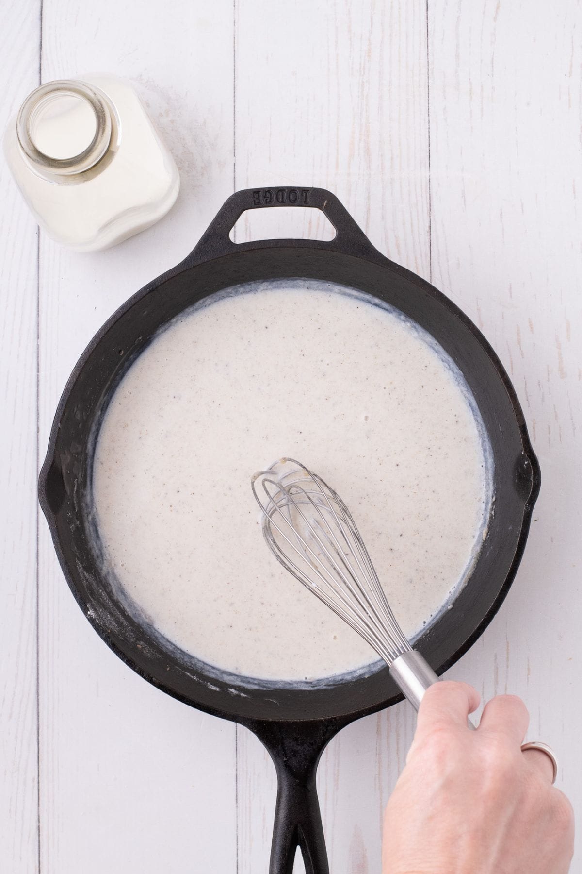 A hand is whisking gravy in a cast iron skillet.