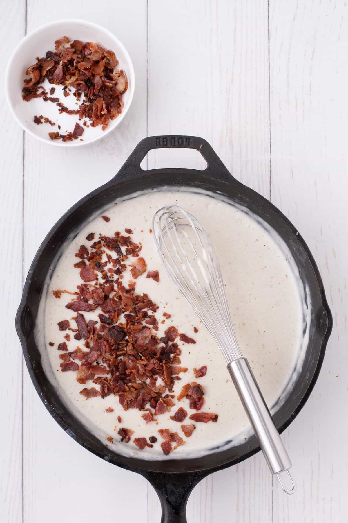 A skillet with bacon gravy and crumbled bacon bits on top.