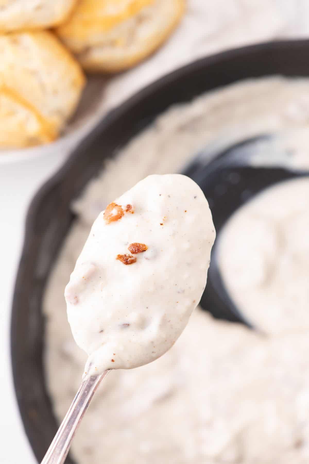 A spoon lifting bacon gravy above the skillet.