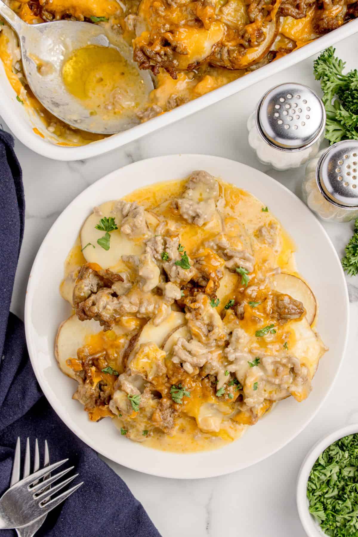 A white dinner plate with a serving of cheesy hamburger potato casserole.