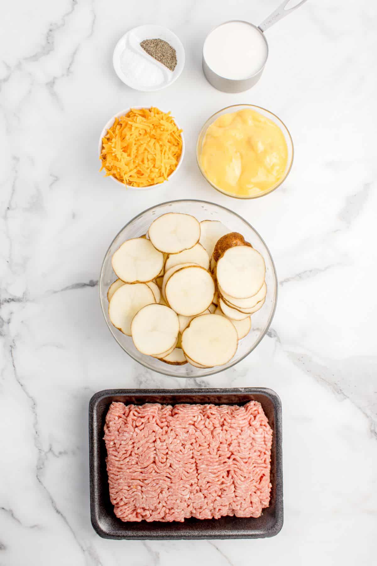 Ingredients for cheesy hamburger potato casserole: salt, pepper, milk, cheddar cheese, cream of chicken soup, sliced potatoes, and ground beef.