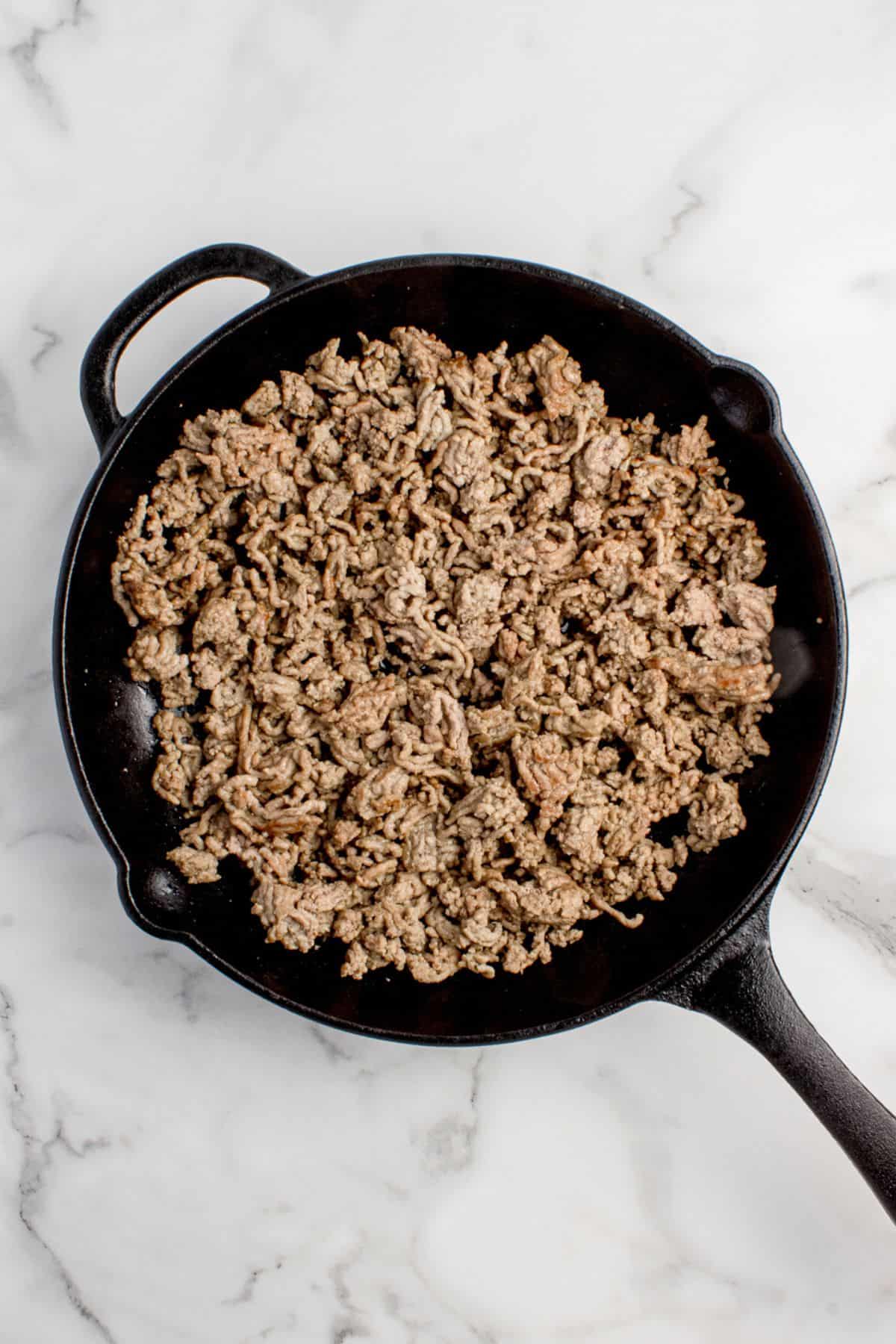 A cast iron pan with cooked ground beef in it.