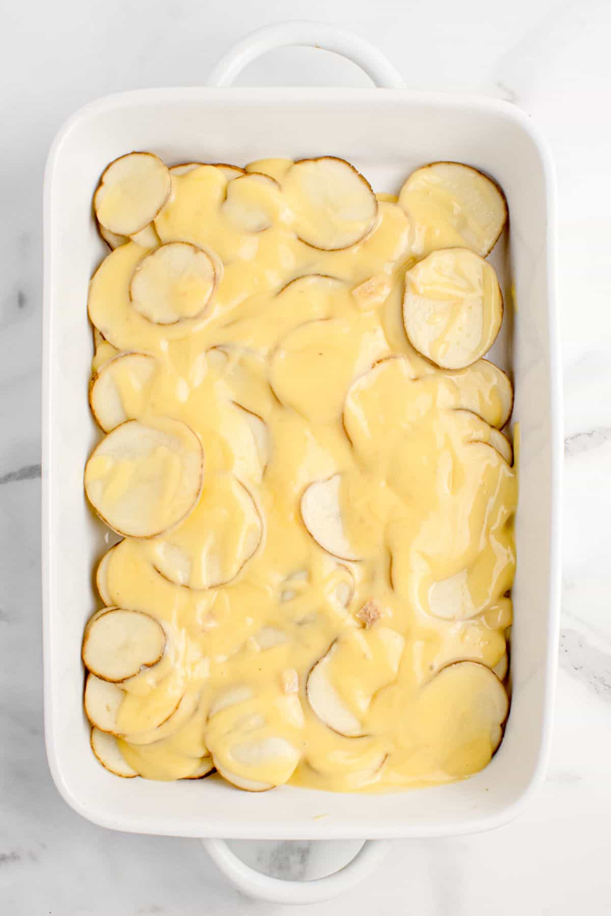 A white baking dish with a layer of sliced potatoes and cream of soup mix.