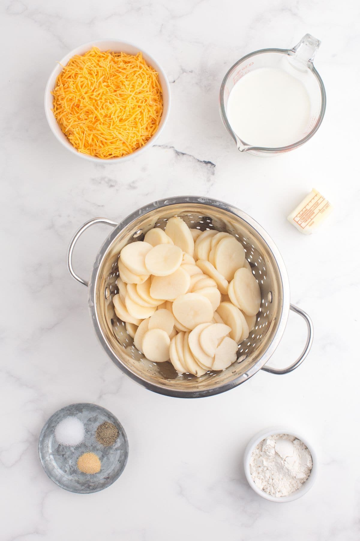 Ingredients for easy scalloped potatoes: Canned sliced potatoes, milk, butter, cheddar cheese, flour, salt, garlic, and black pepper.
