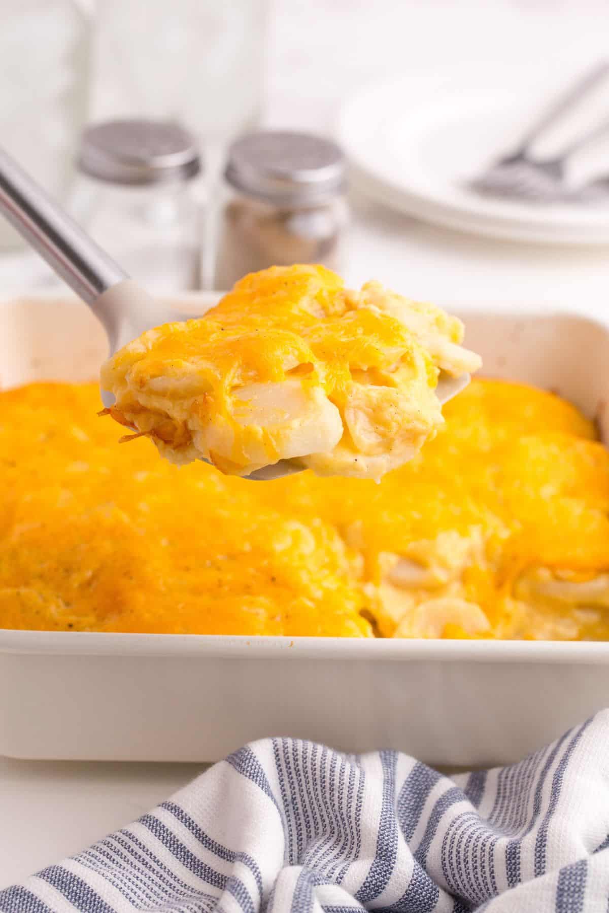 A serving spatula lifting a portion of scalloped potatoes above the baking dish.