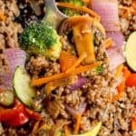 Stir fry on a serving spoon lifted above the cast iron pan.