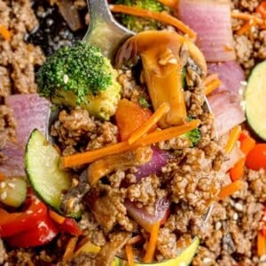 Stir fry on a serving spoon lifted above the cast iron pan.