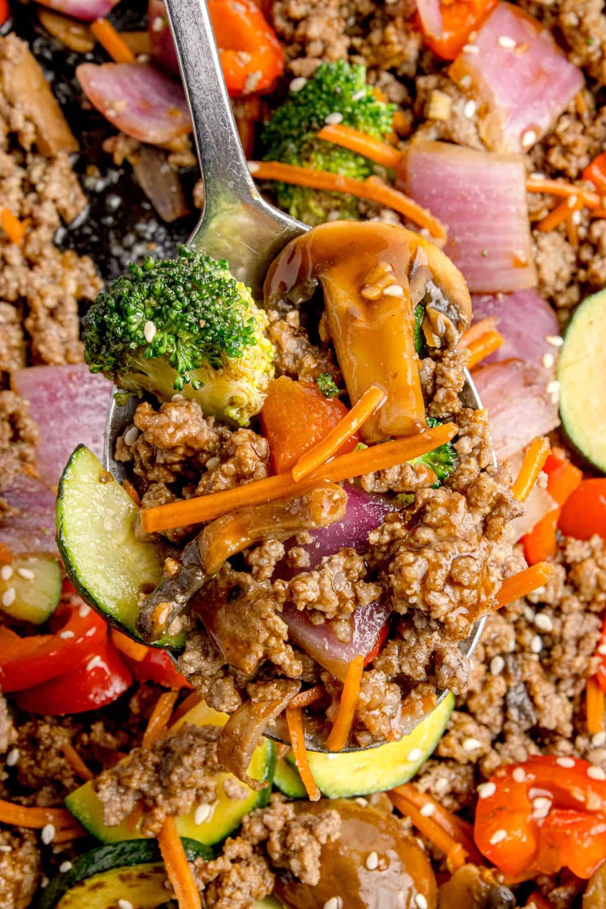 Stir fry on a serving spoon lifted above the cast iron pan.