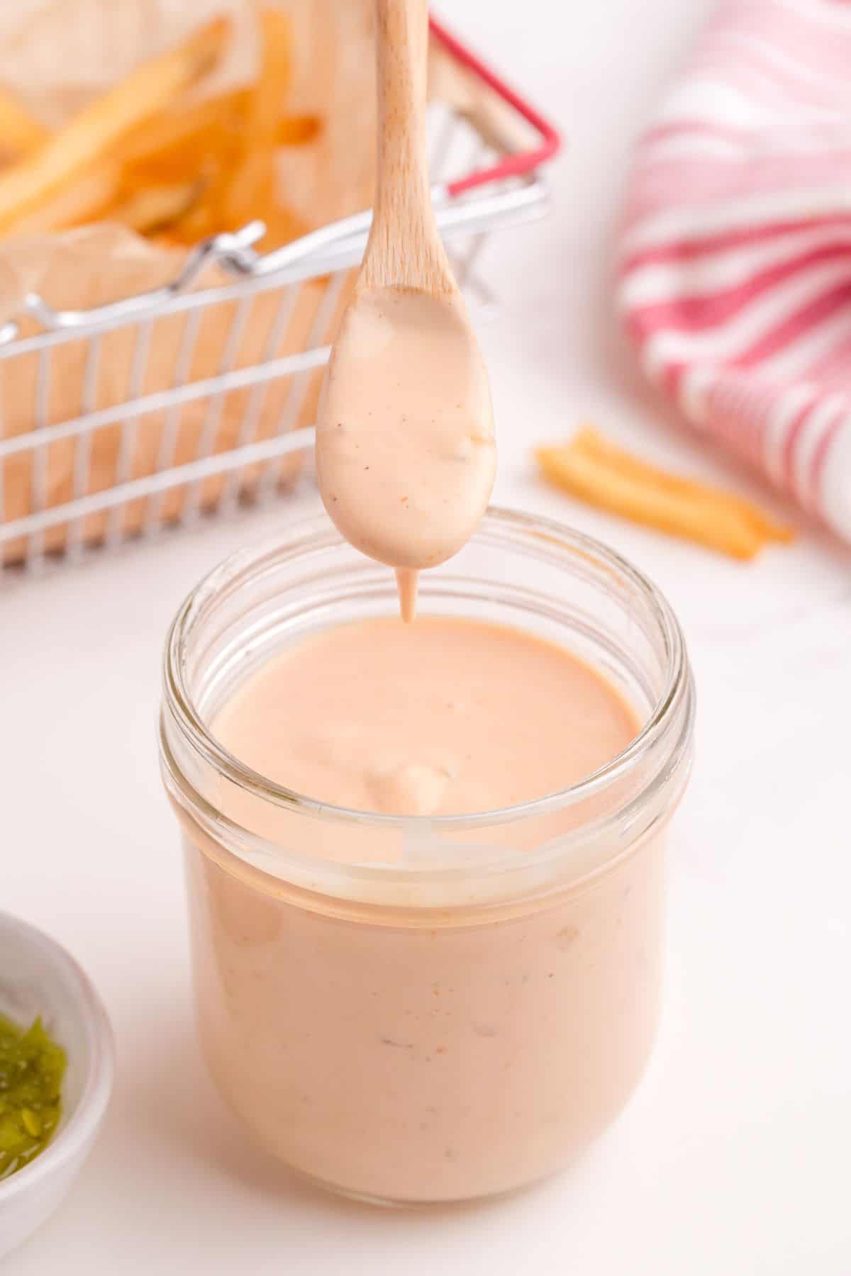 A wooden spoon is lifting some of the In-N-Out sauce out of the clear glass mason jar.