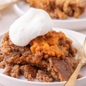 A serving of pumpkin dump cake on a white plate with a dollop of whipped cream.