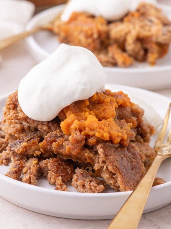 A serving of pumpkin dump cake on a white plate with a dollop of whipped cream.