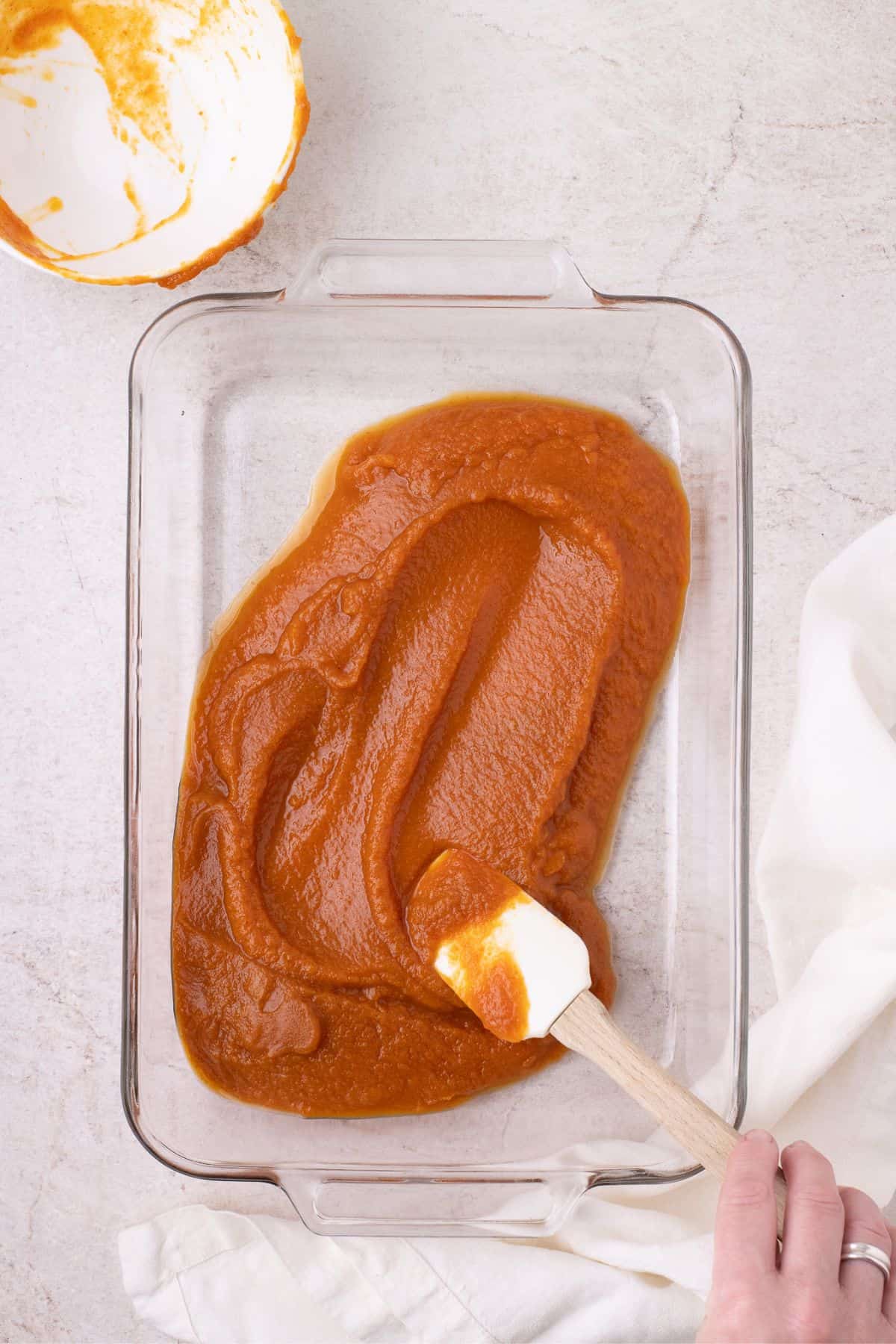 Pumpkin pie filling is evenly spread over the bottom of the glass baking sheet.