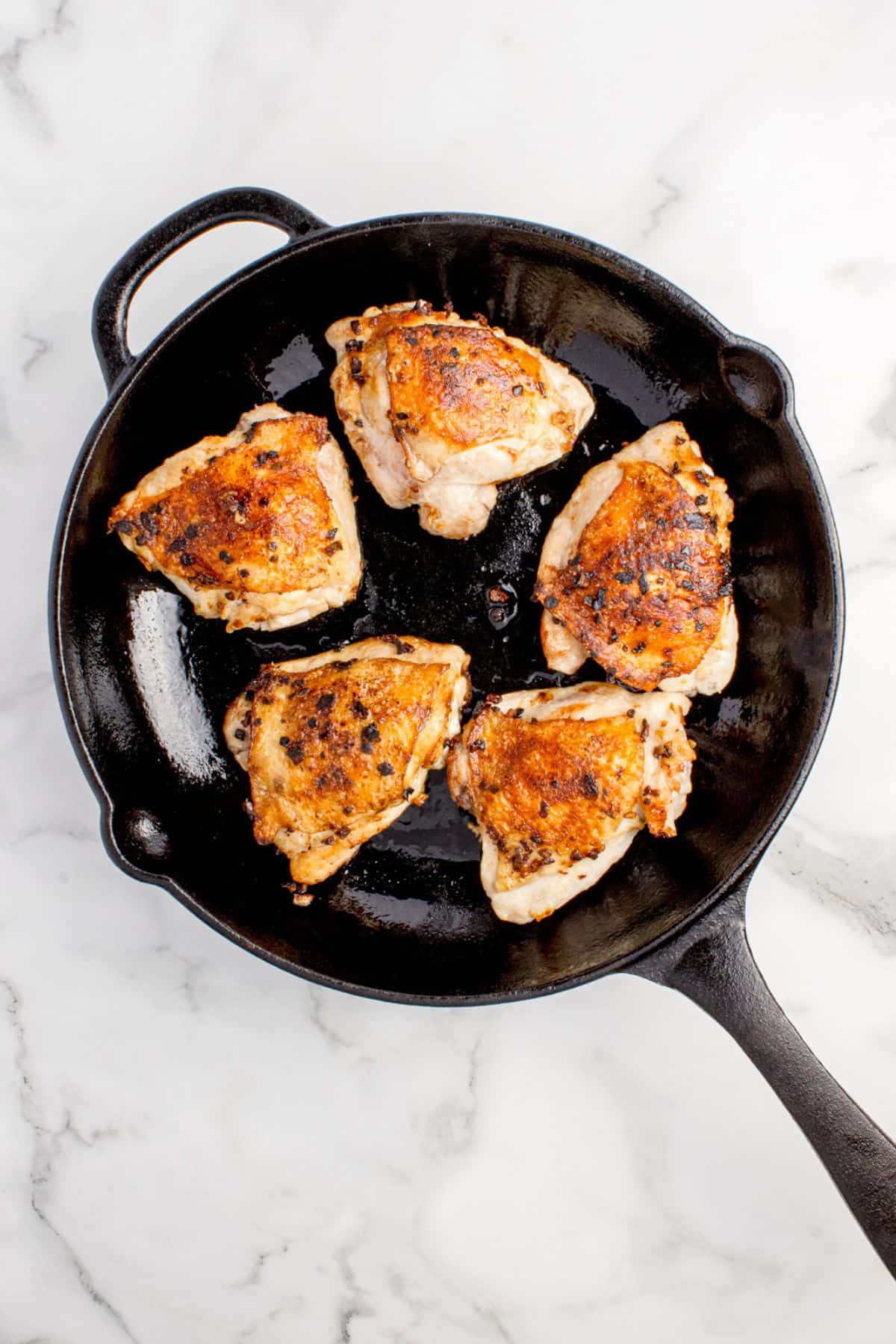 Chicken thighs are browned in a cast iron pan.