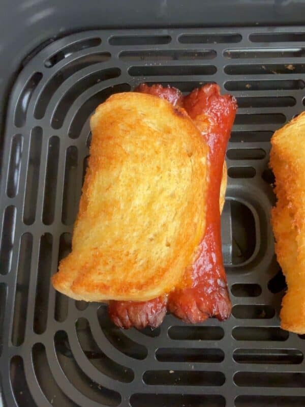 Closeup of the air fryer grilled cheese hot dogs to show the golden brown on the outside, in an air fryer basket.