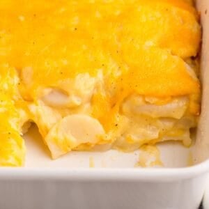 Easy scalloped potatoes in a casserole dish with a section cut out to see the inside of the potatoes and cheesiness.