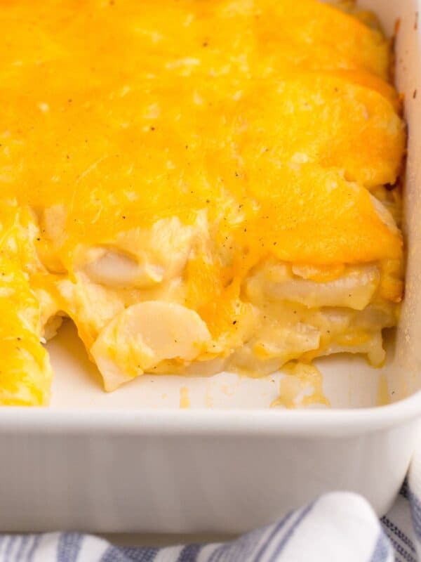 Easy scalloped potatoes in a casserole dish with a section cut out to see the inside of the potatoes and cheesiness.