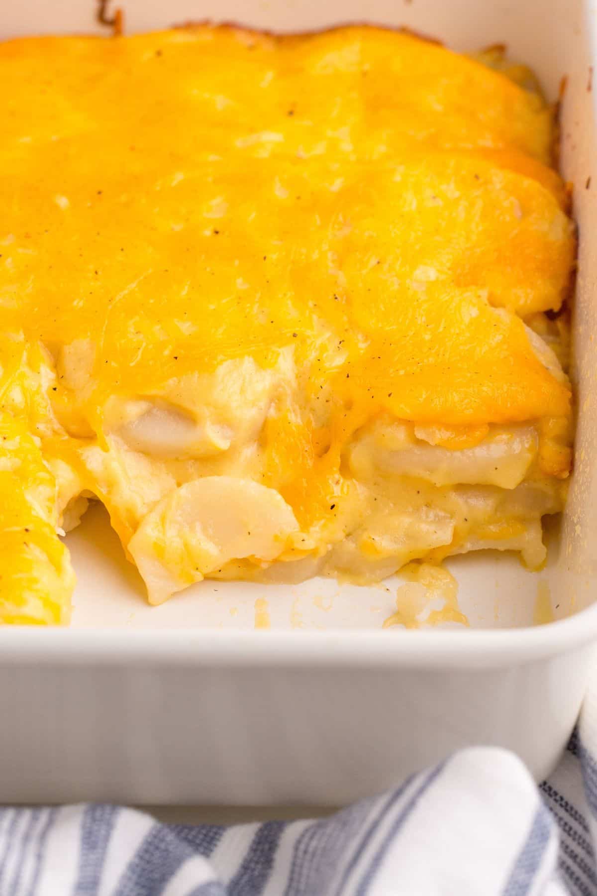 Easy scalloped potatoes in a casserole dish with a section cut out to see the inside of the potatoes and cheesiness.