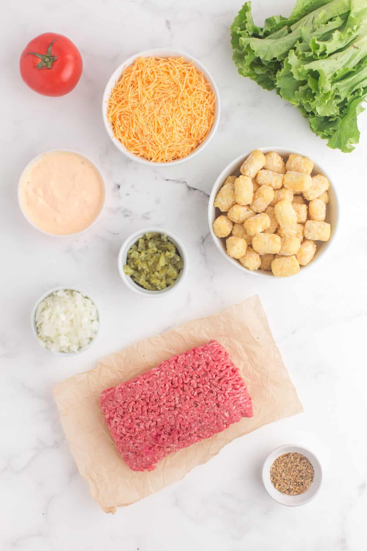Ingredients for big mac casserole: ground beef, tater tots, onion, burger seasoning, dill pickles, homemade Big Mac Sauce, cheddar, lettuce, and tomatoes.