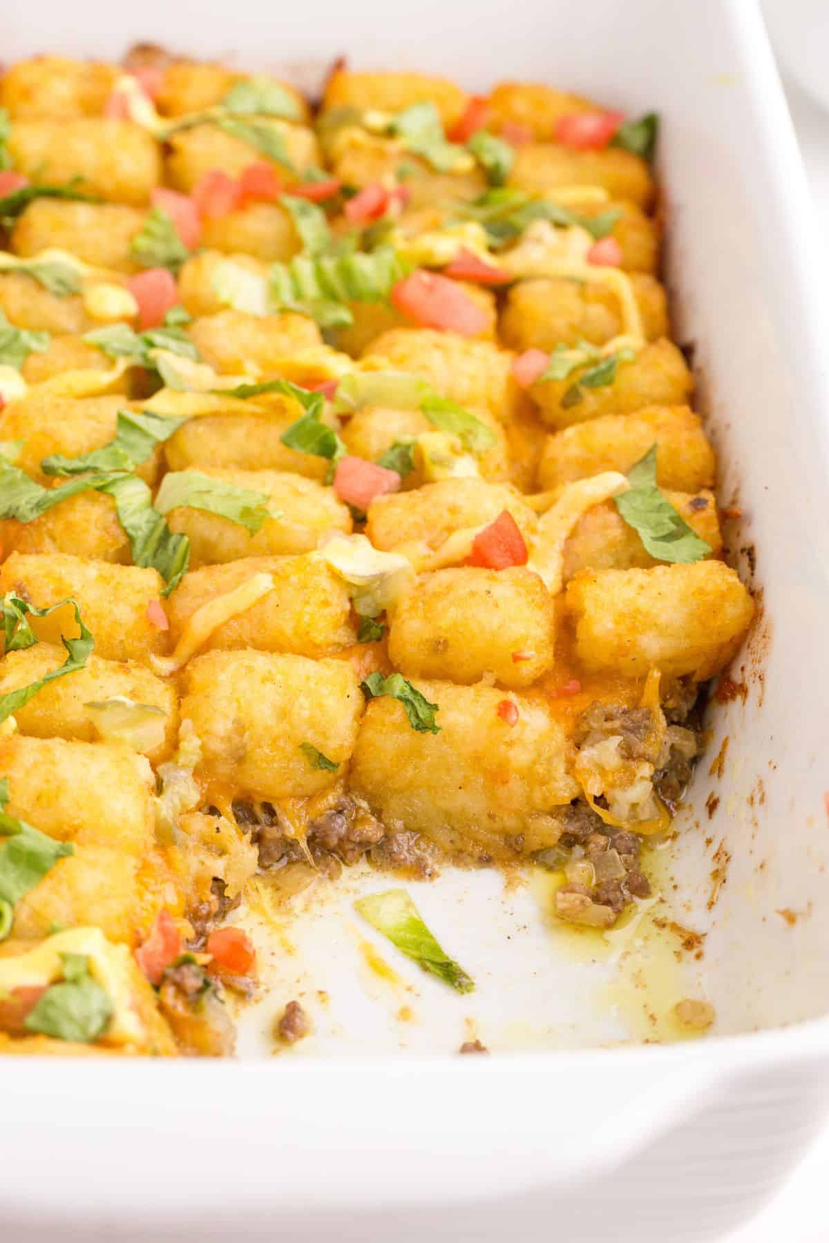 A white baking dish with big mac casserole. A portion has been removed from the corner of the baking dish.